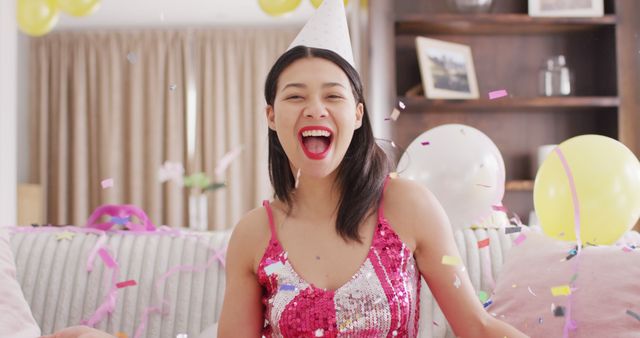 Image of smiling biracial woman in party hat and dressed in pink dress. Party, leisure time, domestic life and lifestyle concept.