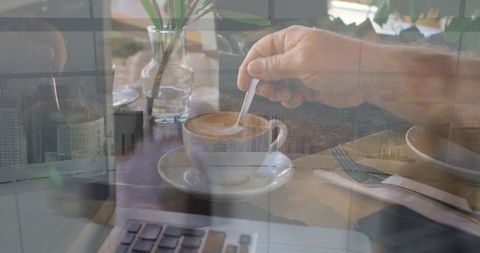 Stirring cappuccino at urban workstation with laptop and city skyline double exposure