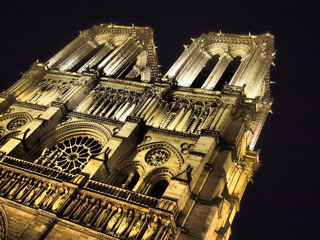 A grand Gothic cathedral's illuminated facade at night highlighting the intricate architectural detail. This visually striking image is perfect for travel blogs, architectural studies, art projects, and promotional materials focused on European tourism or historical sites.