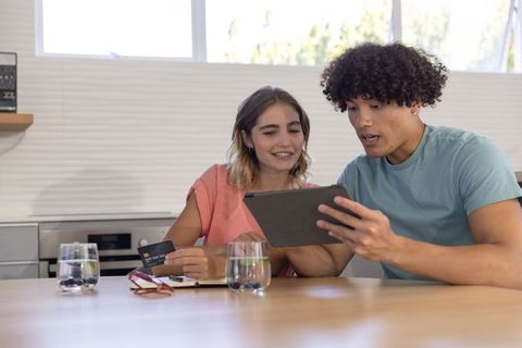 Young couple comparing credit card while reviewing tablet at modern kitchen table