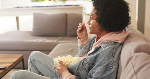 African american man relaxing on sofa eating popcorn watching tv in sunlit living room