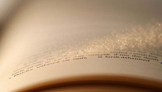 Open book page catching warm golden glitter sparkles, macro bokeh, paper texture