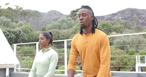 Diverse friends practicing mindful breathwork on balcony overlooking mountains