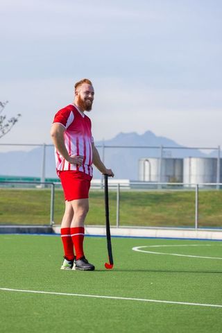 Bearded male athlete holding field hockey stick on turf