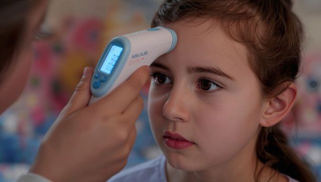 Girl having forehead temperature measured with infrared thermometer at home