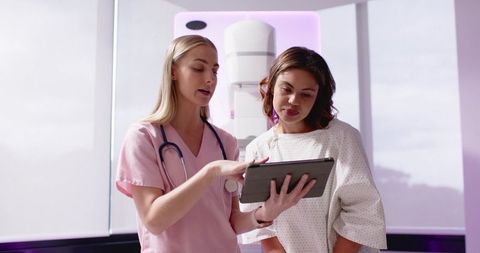 Nurse explaining mammogram results to patient using tablet in radiology suite, purple glow