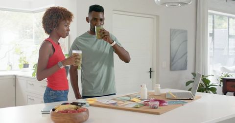 Couple planning home makeover with vision board while sipping green smoothies in kitchen