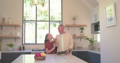 Sunlit modern farmhouse kitchen couple sharing moment at marble island with tablet