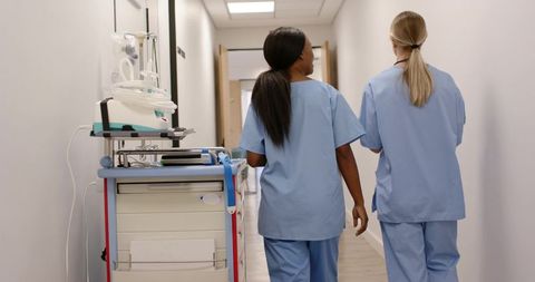 Female nurses walking down hospital corridor pushing medical cart during rounds