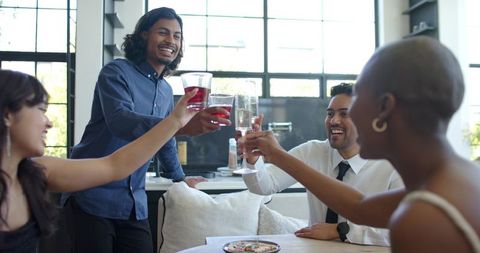 Friends toasting in modern loft, clinking glasses during sunlit urban celebration