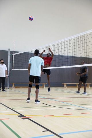 African american men playing indoor volleyball jumping and spiking ball on gym court