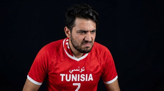 Scowling tunisian football fan wearing tunisia #7 jersey expressing intense focus