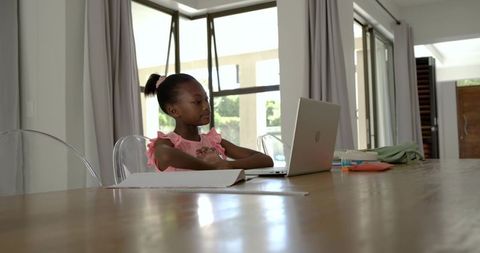 African american girl studying at home with laptop and notebook in sunlit modern interior
