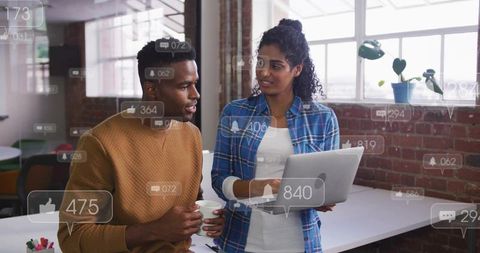 Coworkers Collaborating Over Laptop in Modern Brick Office with Social Media Notifications