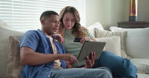 Young couple relaxing on couch shopping online at home using tablet and credit card