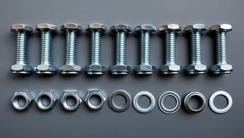 Aligned steel hex bolts with nuts and washers on grey background