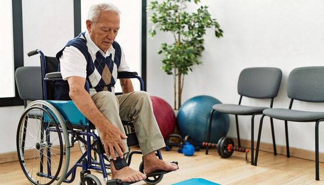 Senior man adjusting ankle support in wheelchair during rehabilitation session at clinic