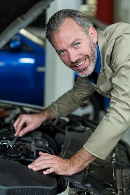 Mechanic smiling while servicing a automobile car engine in repair garage