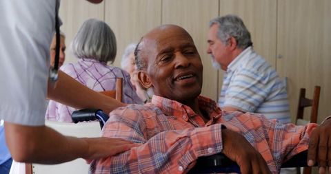 Senior man relaxing in wheelchair while caregiver offering comforting touch in community lounge