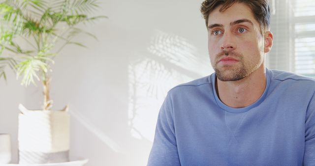 Man seated in modern room with natural light casting shadows. Perfect for use in ads, blogs, or websites related to lifestyle, home decor, mental health, or fashion.