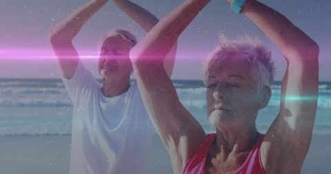 Senior couple practicing gentle beach yoga and morning stretching with lens flare