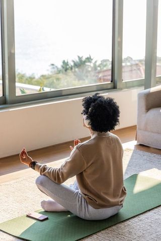 Sunlit home meditation african american woman meditating with headphones and sea view