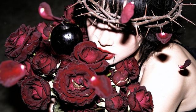 Gothic model wearing crown of thorns holding black apple and deep red rose bouquet