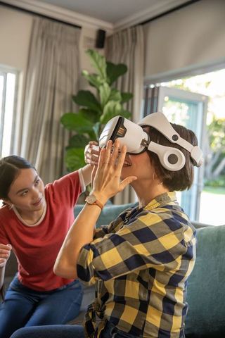 Daughter assisting mother wearing vr headset in comfortable home setting