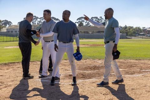 Coach shaking hands starting baseball pregame debrief with players on sunlit diamond field