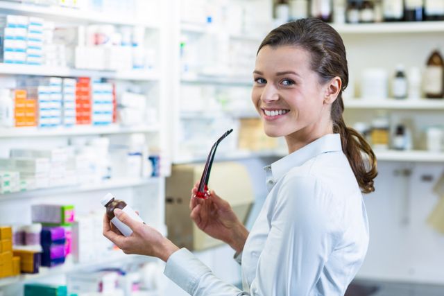 Smiling pharmacist holding a medicine bottle in a well-organized pharmacy. Ideal for use in healthcare-related content, pharmacy advertisements, medical blogs, and articles about pharmaceutical services.
