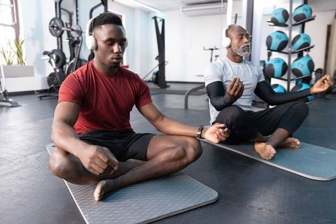 Multigenerational african american men meditating on mats in gym with headphones