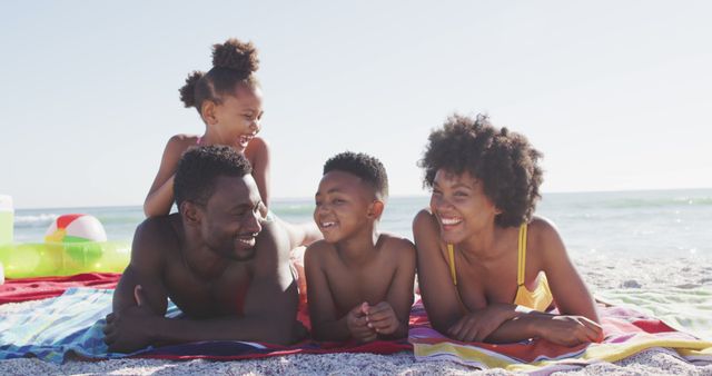 Portrait of smiling african american family lying on sunny beach. healthy, active family beach holiday.