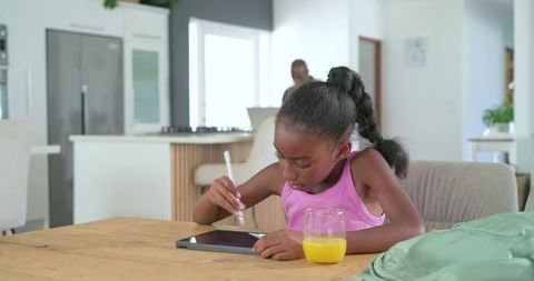 African american girl using tablet with stylus doing homework at kitchen table