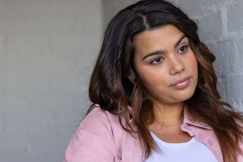 Young woman leaning on gray wall gazing thoughtfully wearing pink shirt and white tank