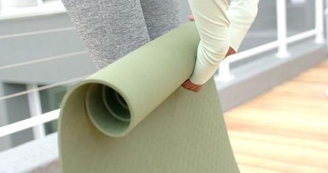 Indian woman carrying pale green yoga mat on balcony preparing for outdoor yoga