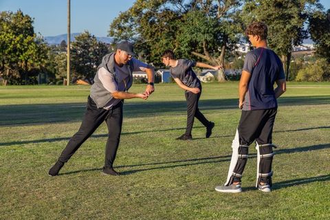 Coach demonstrating catching technique to diverse male teammates on park cricket field