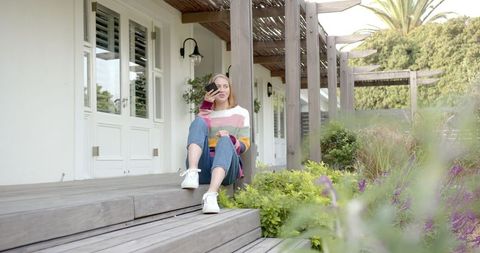 Woman Enjoying Morning Coffee with Smartphone on Charming Porch