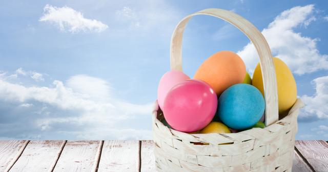 Bright, colorful Easter eggs are in a wicker basket amidst a clean, blue sky with fluffy white clouds. Ideal for holiday greeting cards, seasonal promotions, and festive social media posts promoting springtime celebrations and Easter events.
