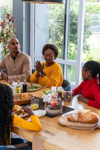 Diverse family sharing sunny home lunch around wooden table with mom in mustard sweater