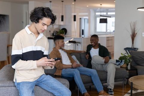 Multiracial teenage friends hanging out in modern living room texting and chatting