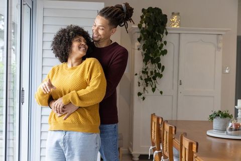 African american couple embracing and smiling in cozy sunlit dining room with shutters