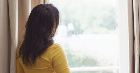 Woman in Yellow Looking Out Window at Home in Leisure Time