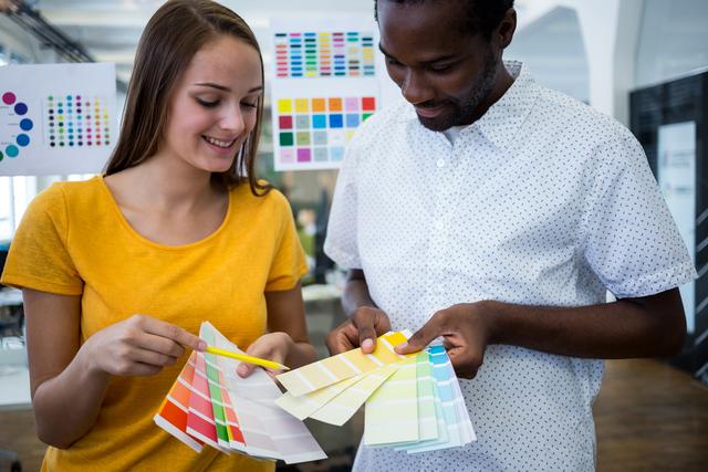 Male and female graphic designers choosing color from the sampler in office