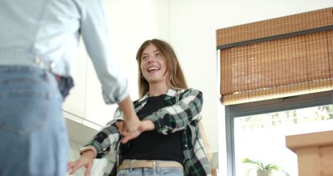 Joyful friends sharing playful kitchen moment laughing and reaching hands in sunlit home