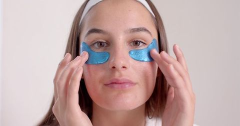 Woman applying blue under-eye gel patches in wellness routine