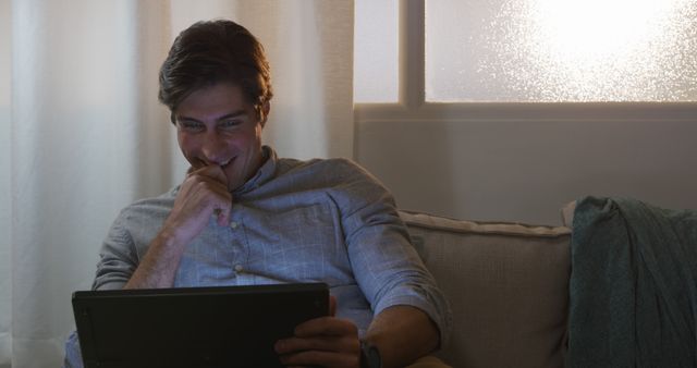 Man Smiling While Using Tablet at Home in Cozy Evening Lighting - Download Free Stock Images Pikwizard.com