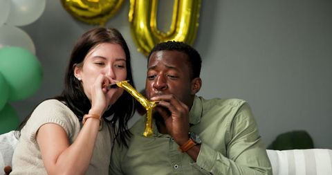 Diverse couple celebrating birthday party with trumpets