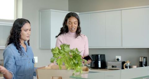 Diverse Friends Unpacking Groceries and Checking Smartphone in Modern Kitchen