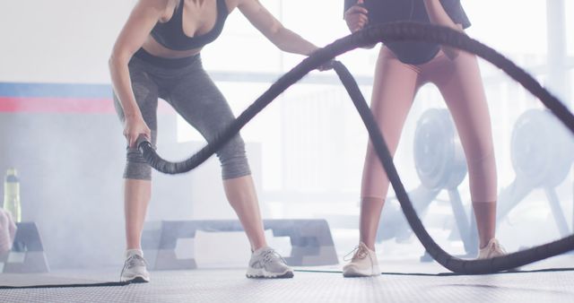 Image of diverse female fitness trainer encouraging woman battling ropes working out at a gym. Exercise, fitness and healthy lifestyle.