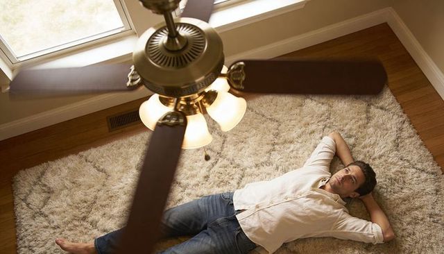 Man lying on shag rug gazing at ceiling fan, casual jeans and beige shirt overhead view